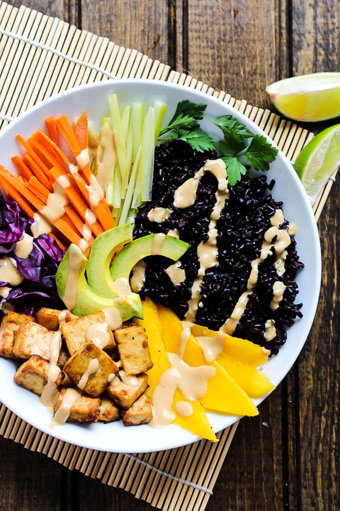 A power bowl filled with tofu, black rice, vegetables, avocado and a tahini sriracha sauce