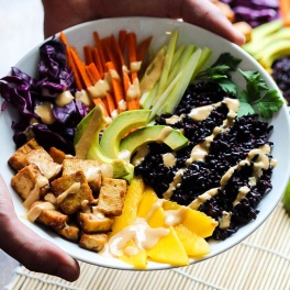 A bowl filled with black rice, avocado, carrots, celery, mango, cabbage and tofu