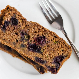 A slice of blueberry zucchini bread served on a white plate with a silver fork