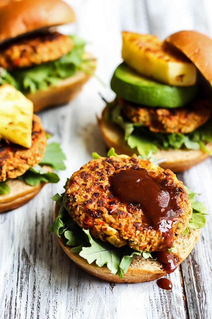 four veggie burgers topped with lettuce, bbq sauce, avocado and pineapple