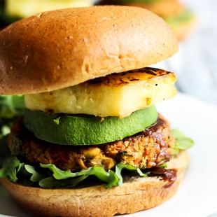 A vegan chickpea patty served on a bun with lettuce, bbq sauce, avocado and grilled pineapple