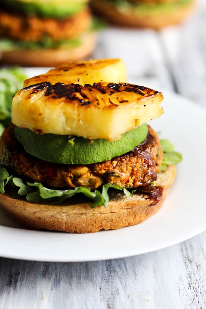 A chickpea veggie burger on a bun with barbecue sauce, avocado and charred pineapple