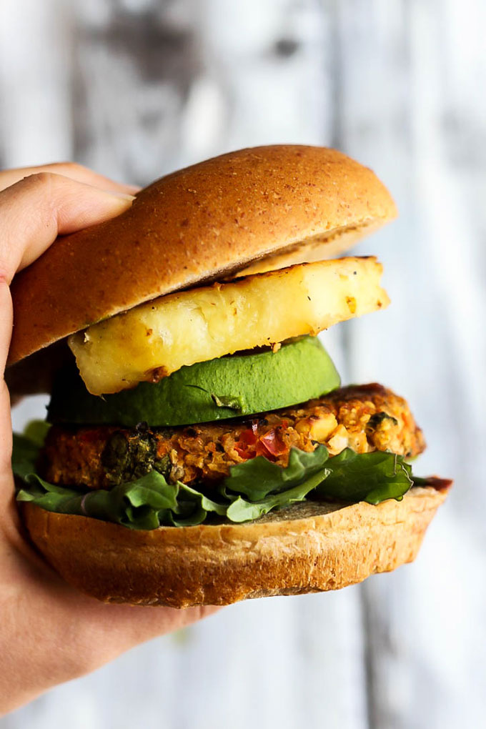 A hand holding a vegan burger with pineapple, avocado and lettuce