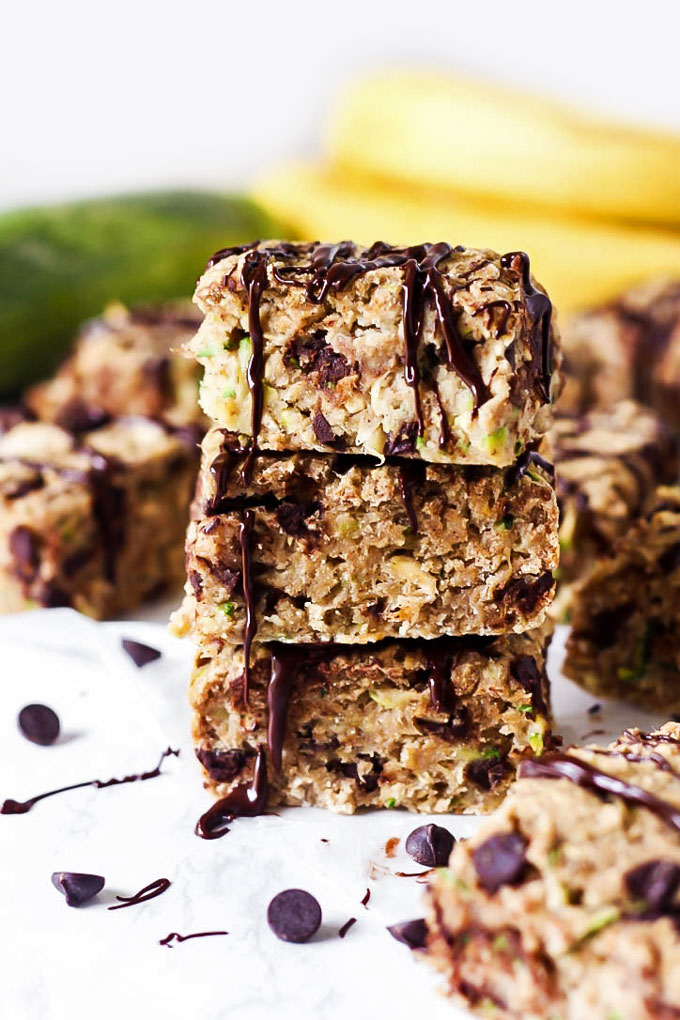 a stack of sliced breakfast bars sitting in front of a zucchini and a bunch of bananas