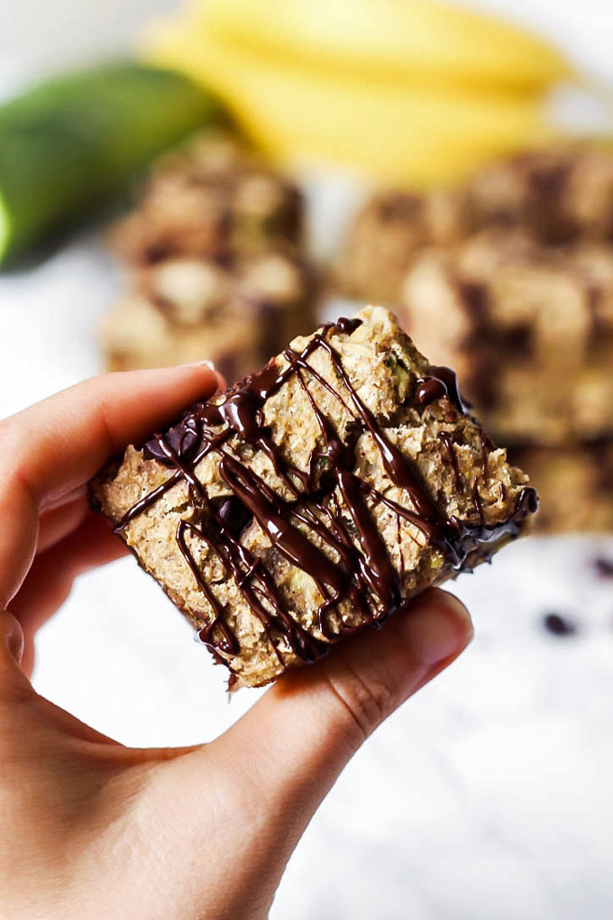 a hand holding a vegan oatmeal breakfast bar topped with a drizzle of chocolate