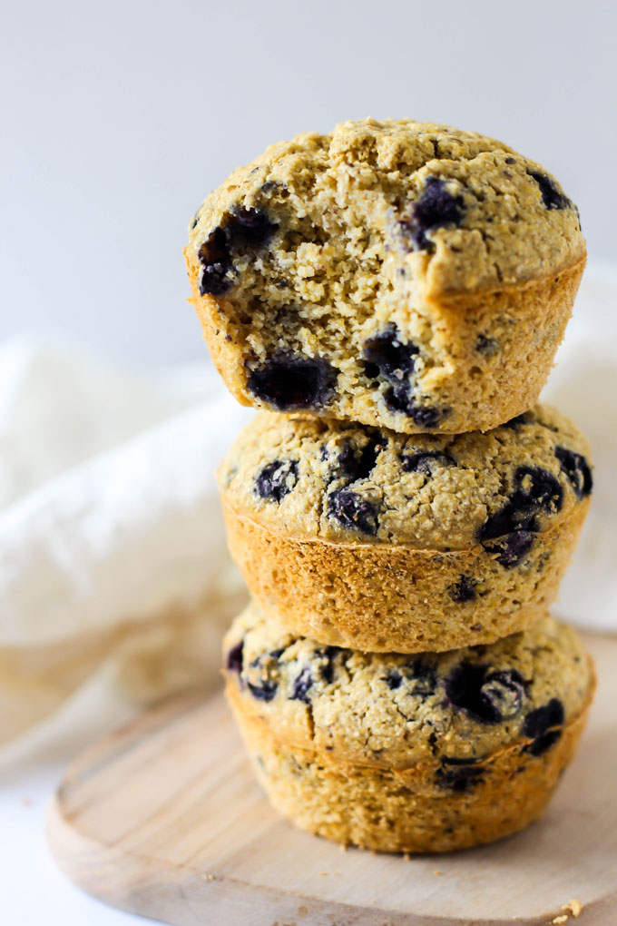 a stack of three blueberry cornmeal muffins, with the top muffin having a bite taken out of it