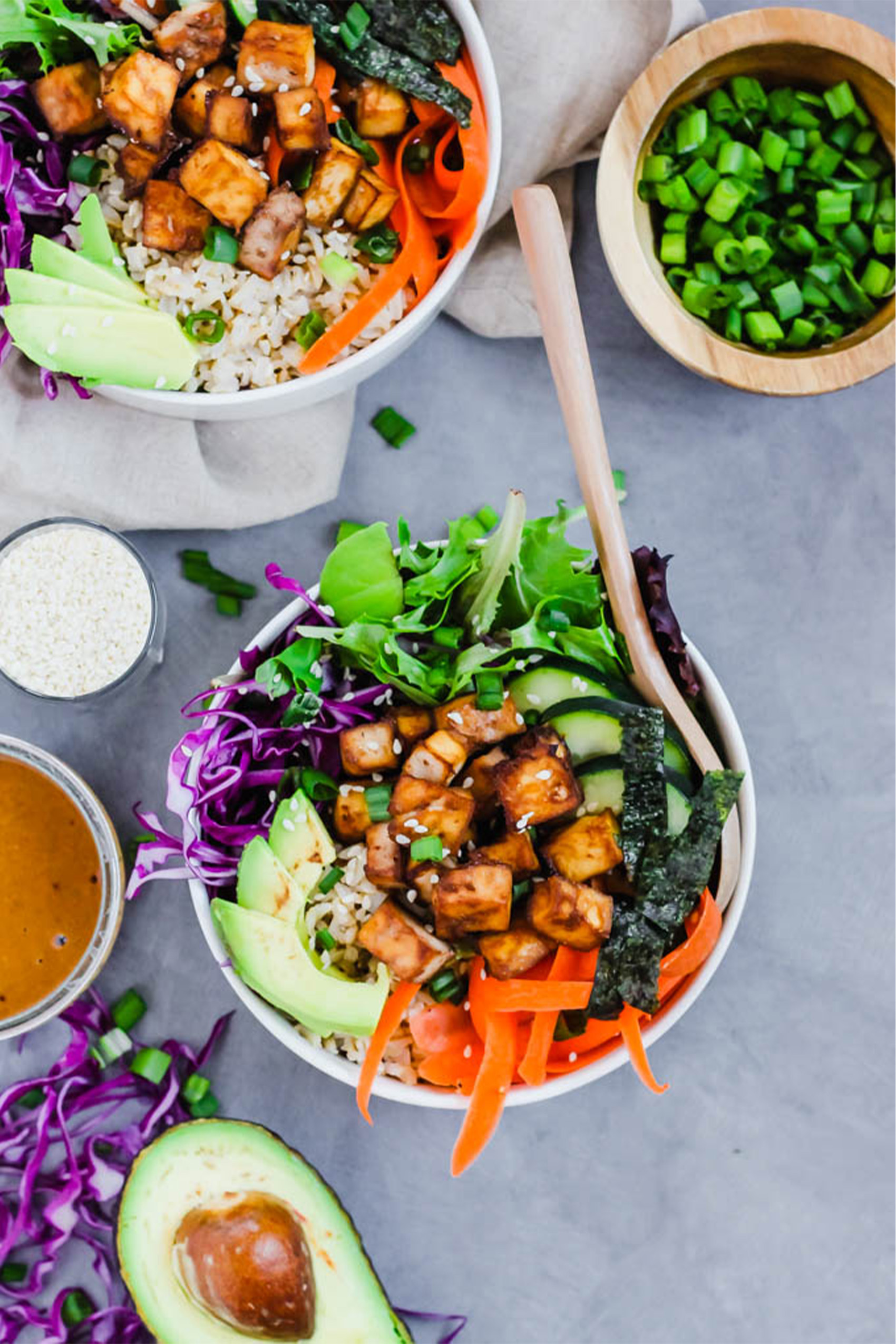 a vegan poke bowl with teriyaki tofu, greens, cucumber, carrots and avocado