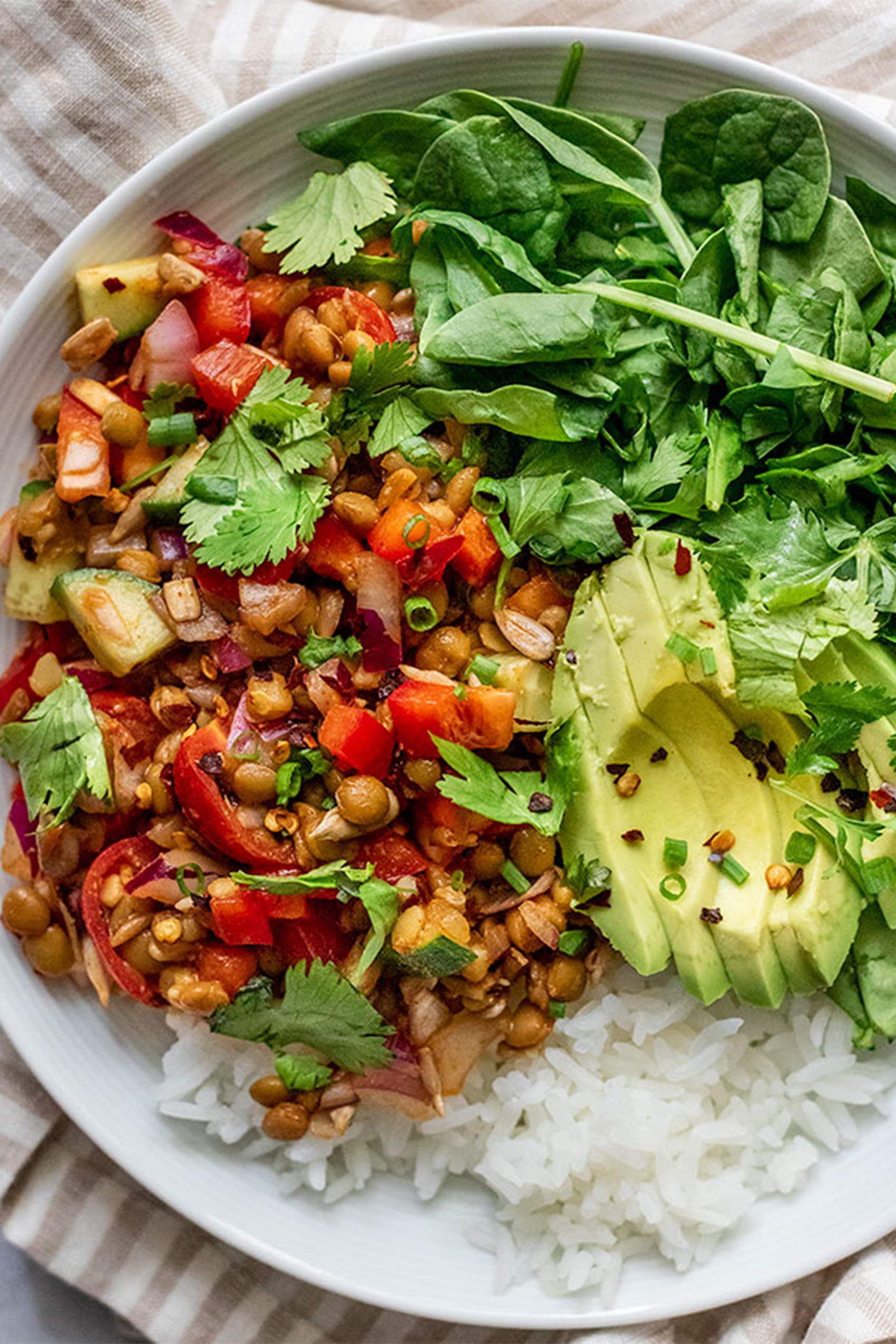 a bowl of rice and greens topped with avocado and cooked veggies and beans