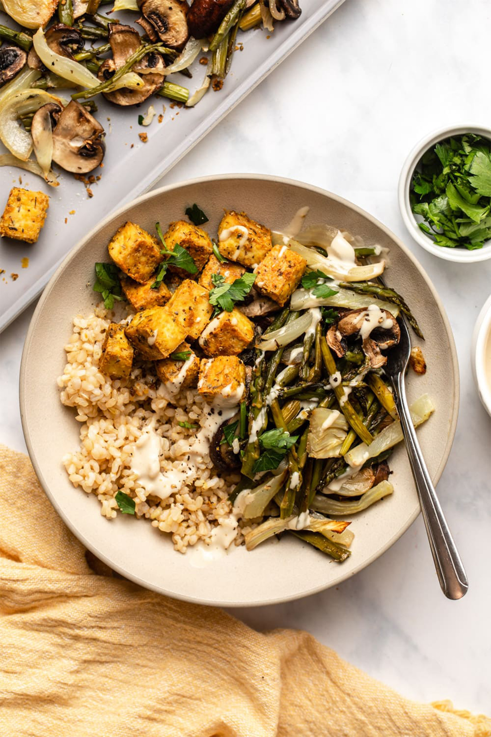 a bowl of grains, tofu and sauteed veggies topped with a creamy tahini sauce