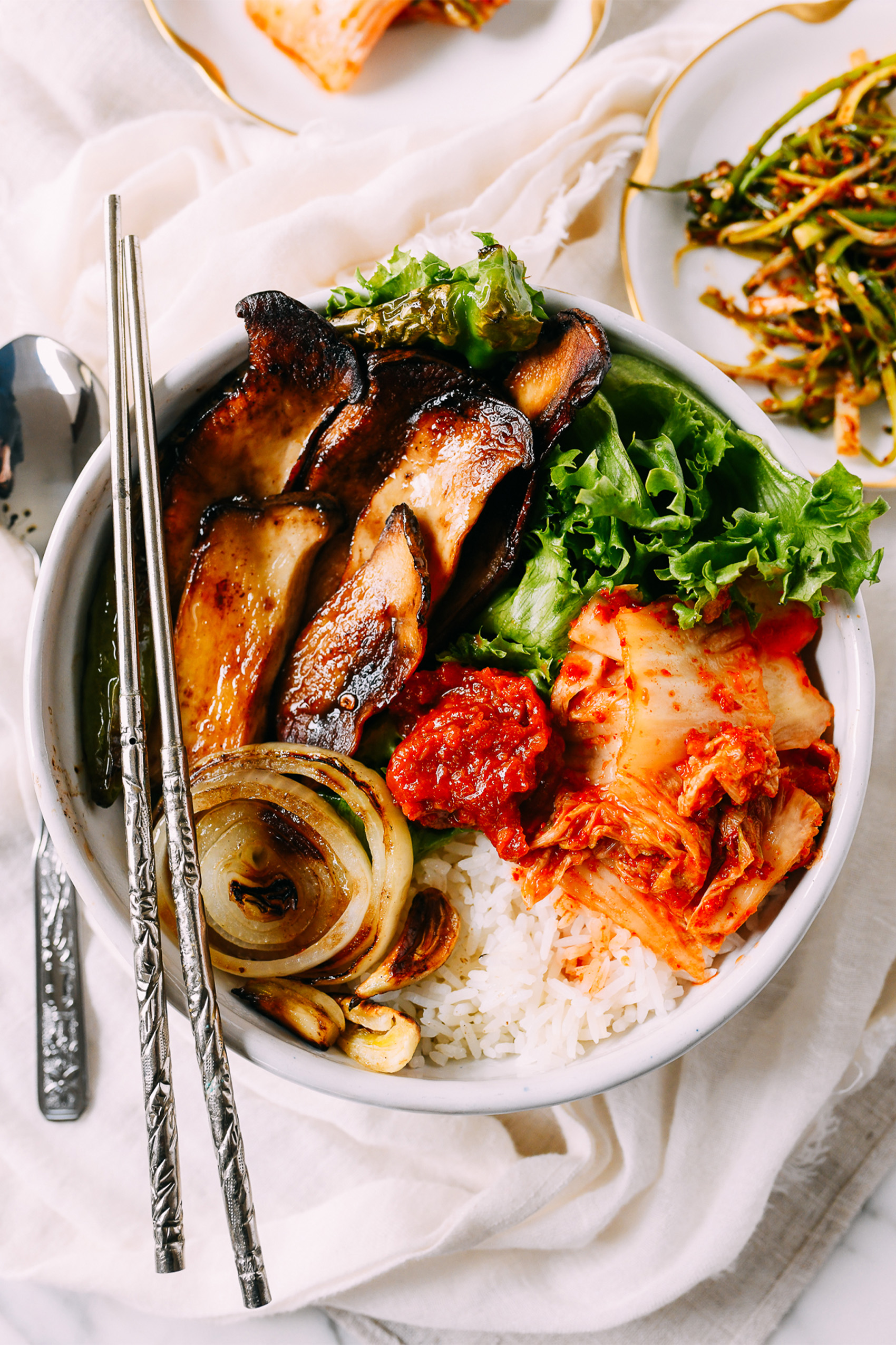 a korean bbq mushroom bowl served over white rice with kimchi and greens