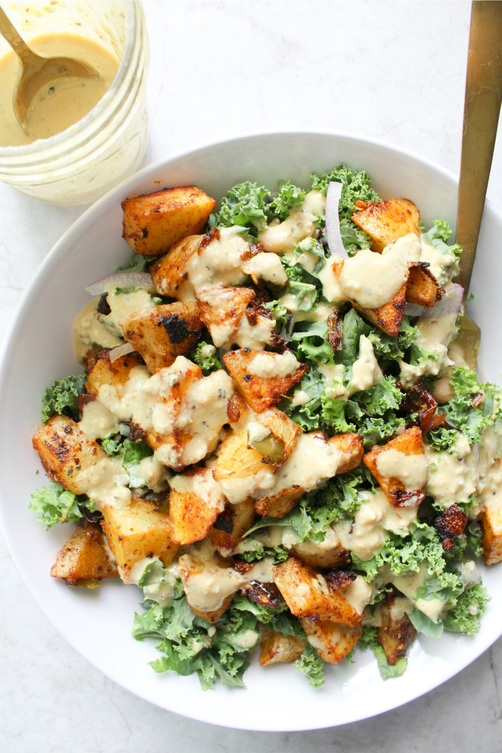 a vegan kale bowl with spicy sweet potatoes and a creamy vegan dressing