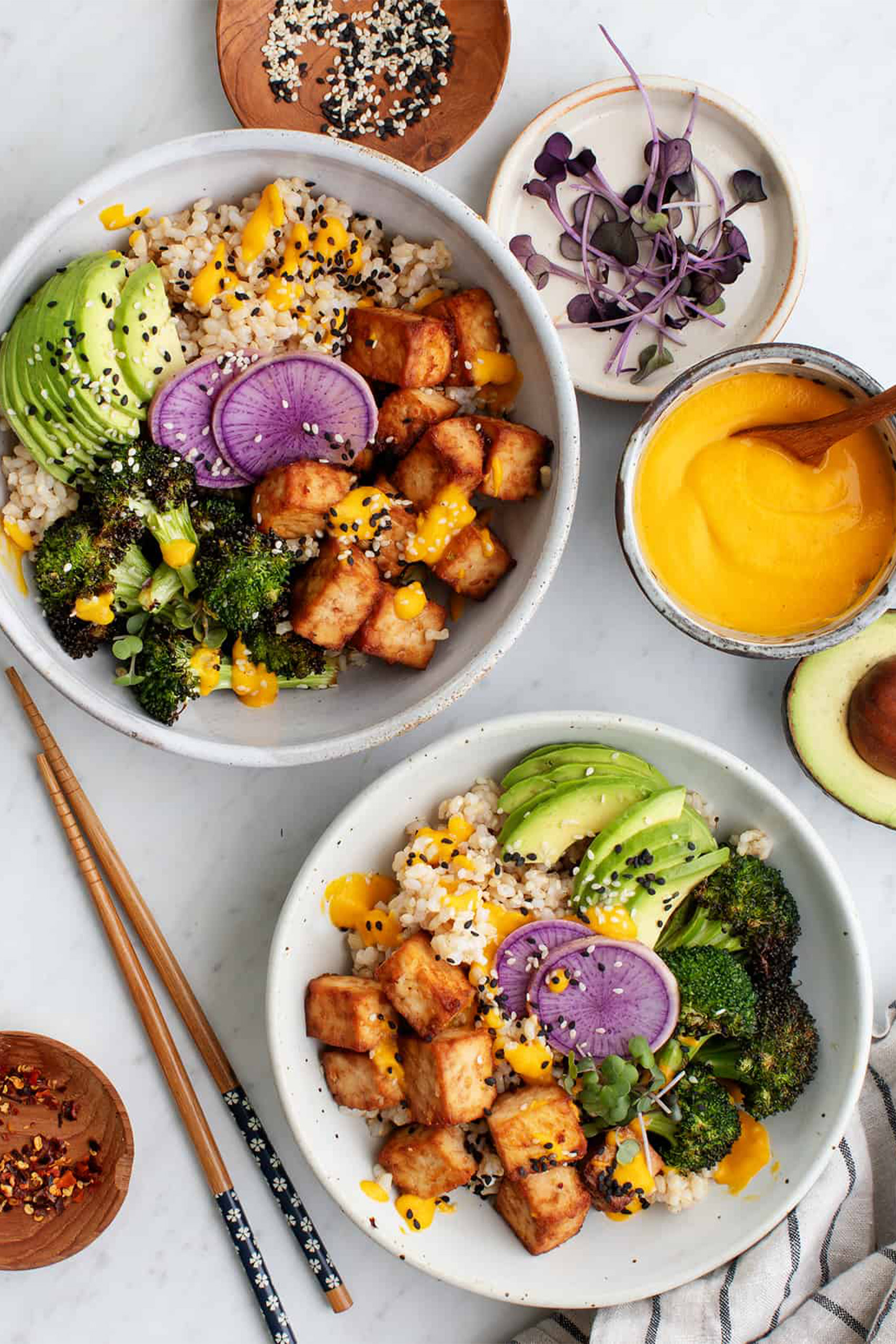 two vegan power bowls with tofu, avocado, brown rice and broccoli with a carrot ginger dressing
