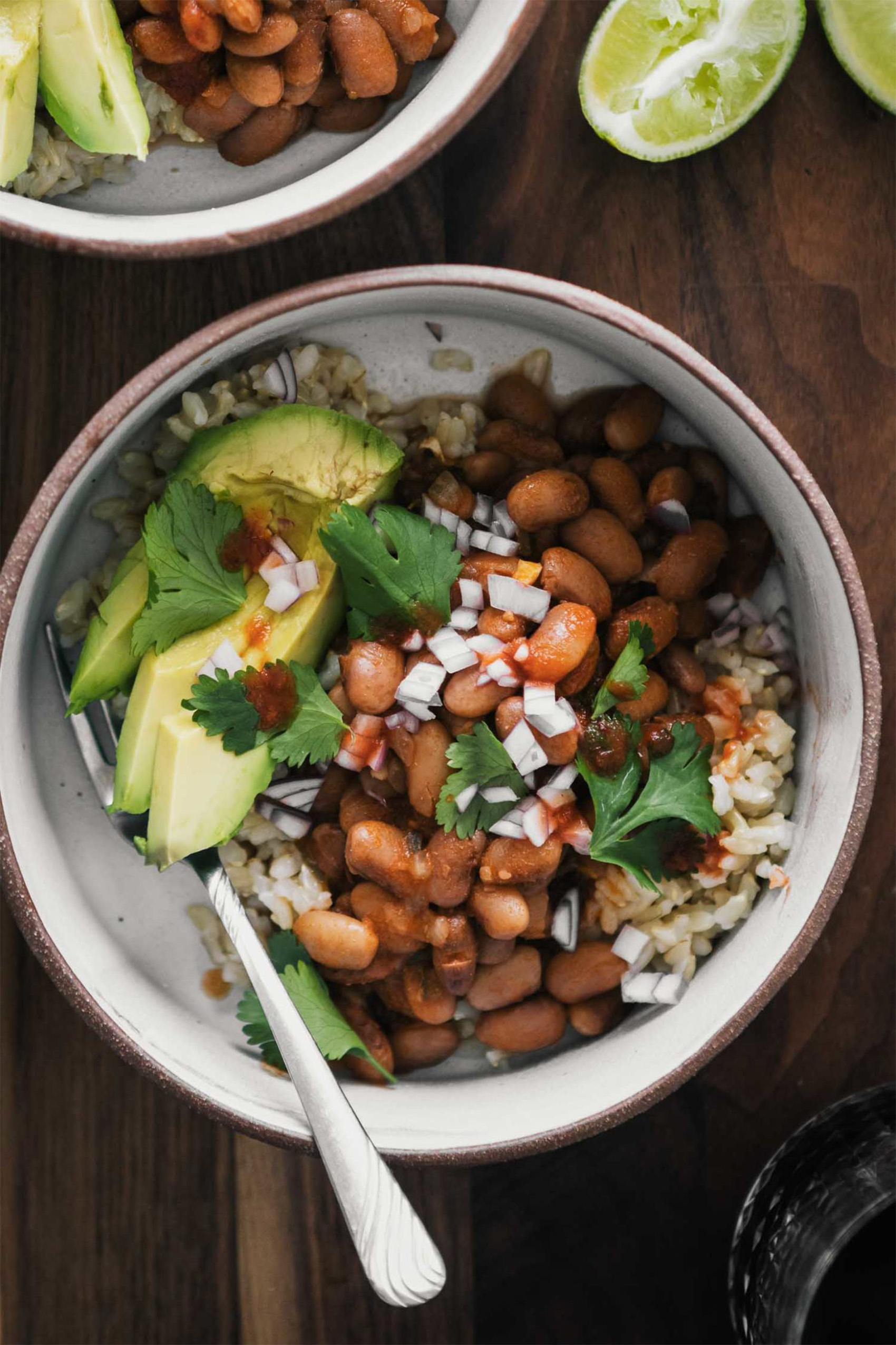 a spicy pinto bean bowl with avocados, onions and brown rice