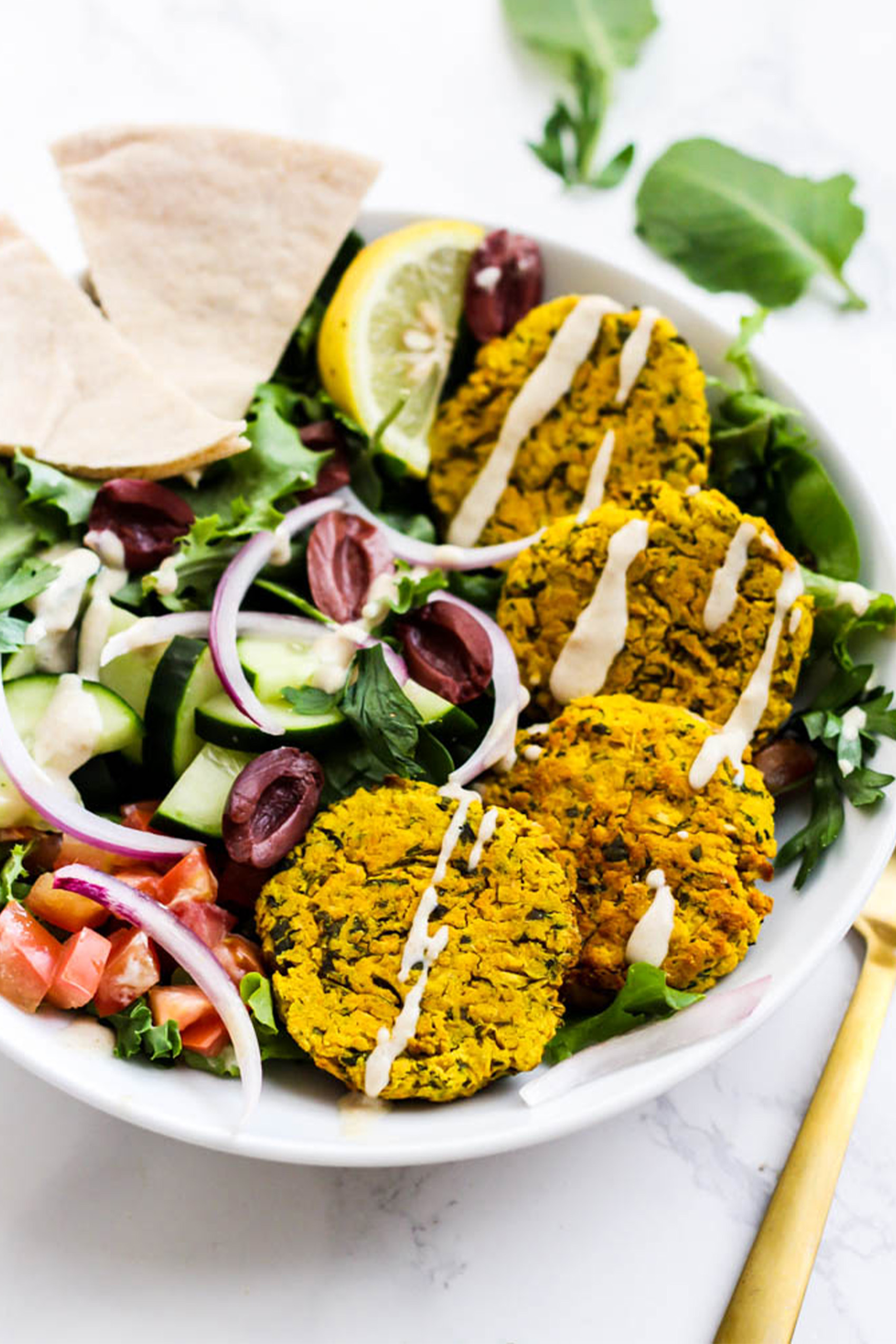 a falafel bowl with four falafel patties served over greens with olives, onions and tomatoes