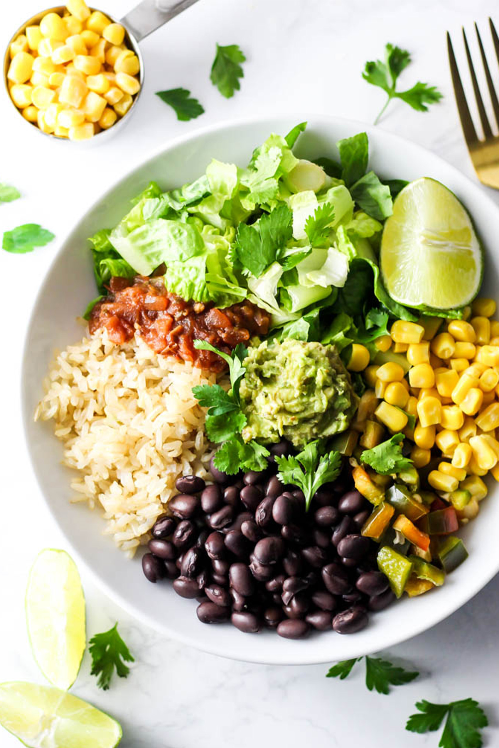 a vegan burrito bowl with rice, black beans, corn, peppers, guacamole and greens