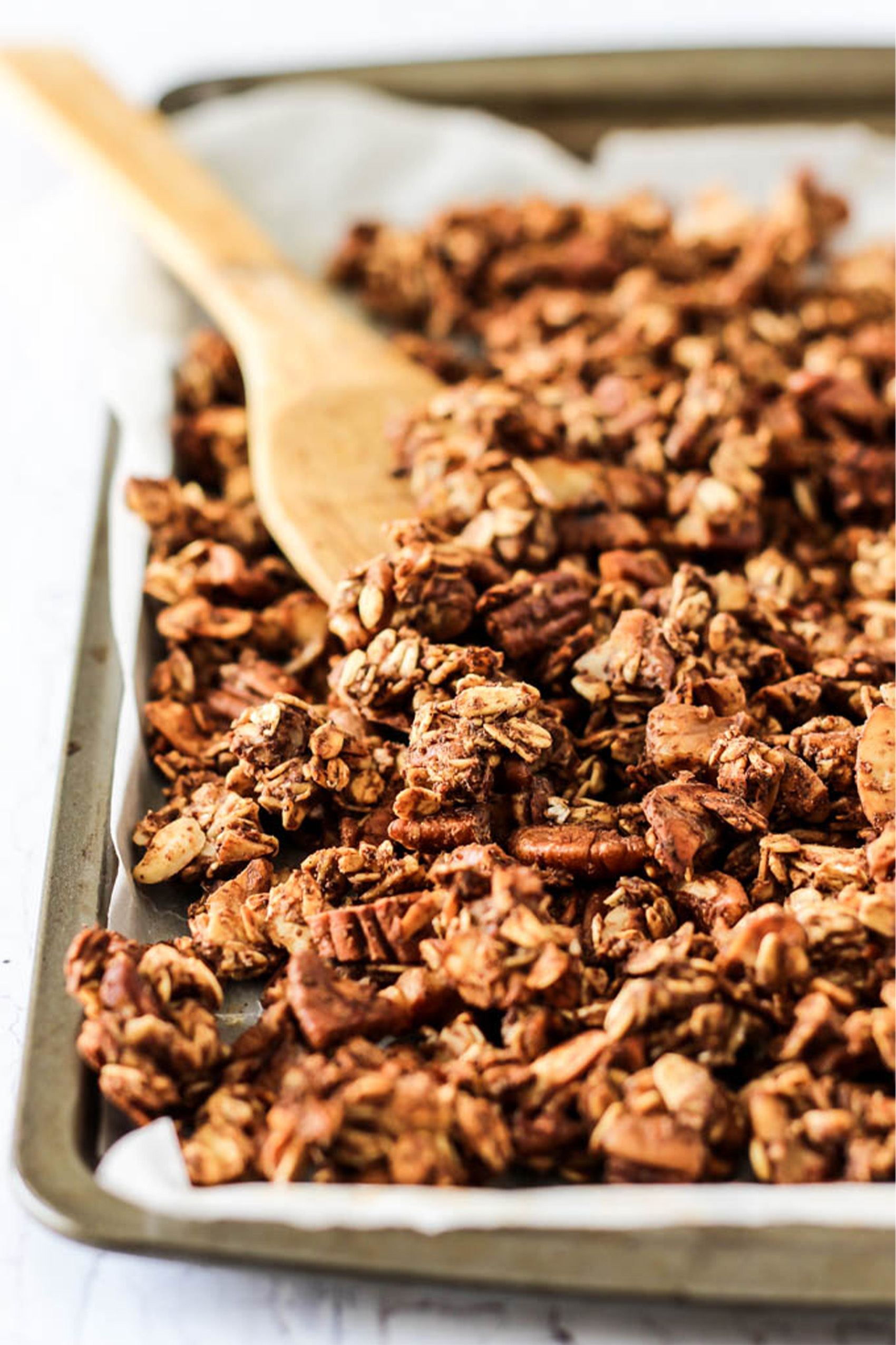 a wooden spoon flipping homemade granola on a sheet tray 