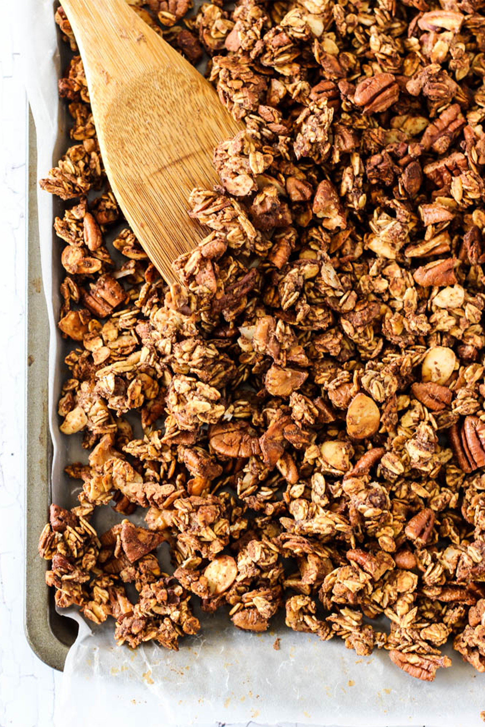 a wooden spoon mixing homemade granola on a sheet tray