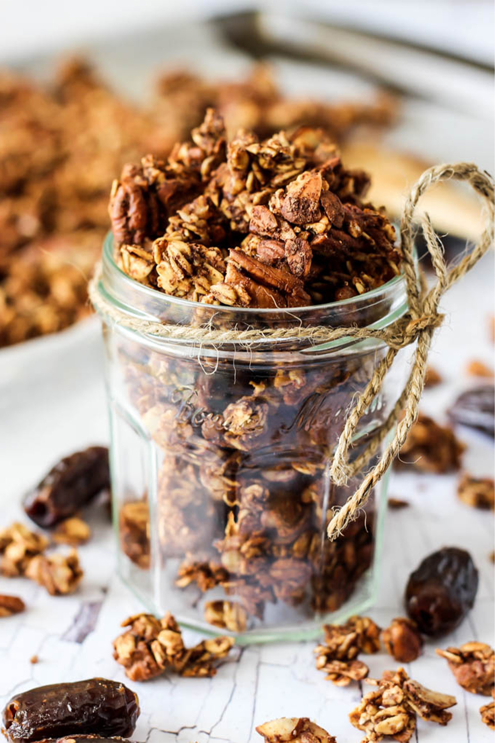 a jar of granola sitting in front of a sheet tray with more granola