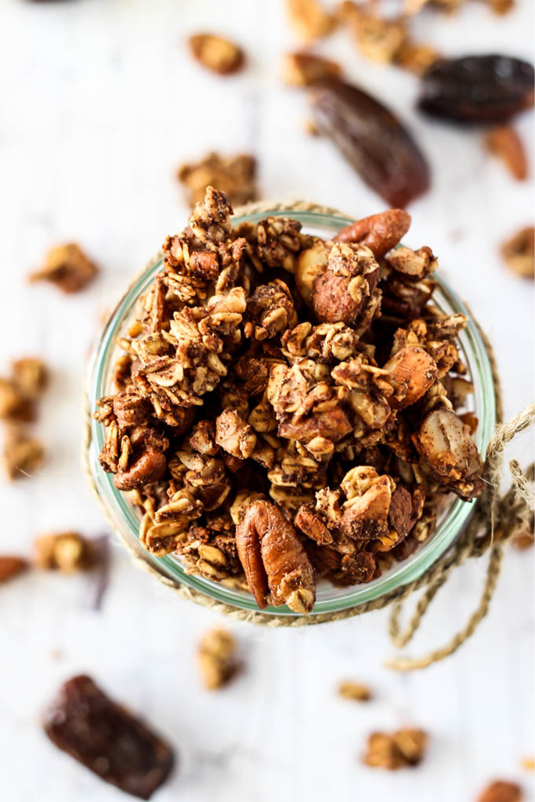 a mason jar filled with homemade granola surrounded by scattered granola clusters