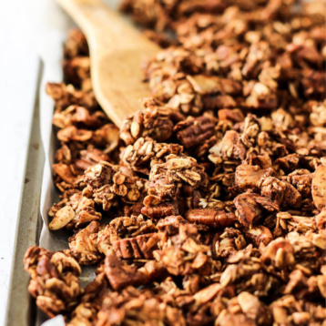 a sheet tray full of homemade chai granola being stirred with a wooden spoon