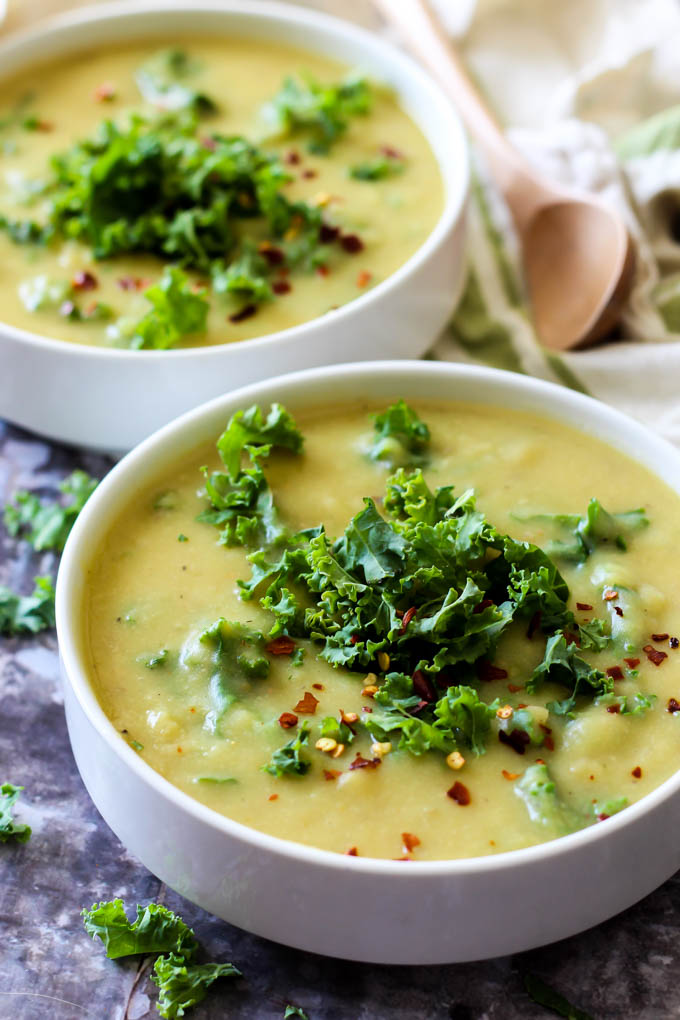 two bowls of potato kale soup topped with red pepper flakes