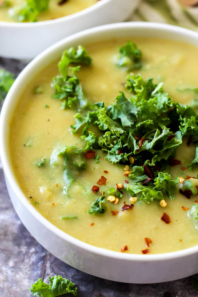 a close up of a bowl of vegan cheesy potato soup topped with kale