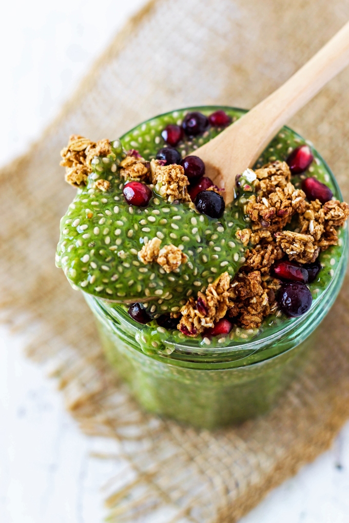 a spoon scooping into a jar of matcha chia pudding topped with granola and berries