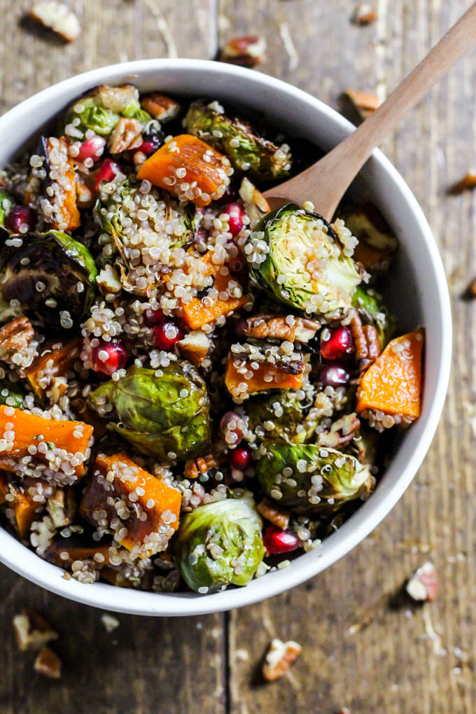 a bowl of warm brussels sprouts salad with quinoa and butternut squash topped with pomegranate seeds and pecans