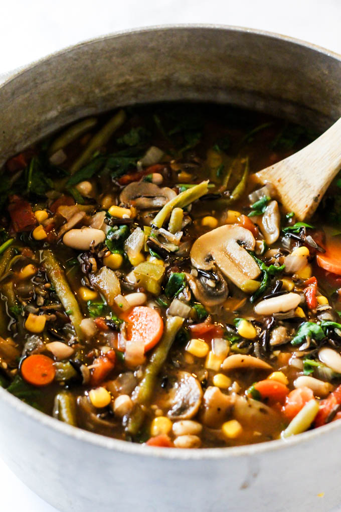 a pot of wild rice vegetable soup being stirred