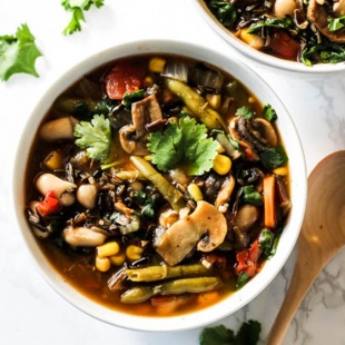 two bowls of vegetable wild rice soup topped with fresh herbs