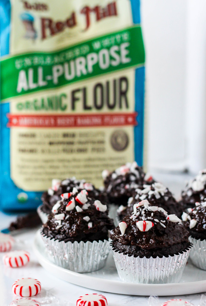 a bag of all purpose flour behind a plate of chocolate cupcakes