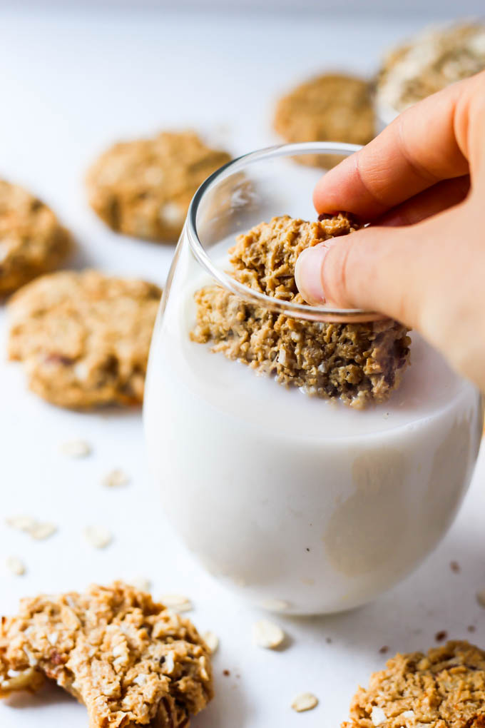 a vegan oatmeal cookie being dunked into a glass of milk