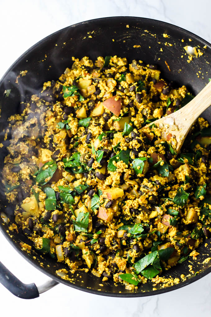 a skillet of tofu scramble being stirred with a wooden spoon