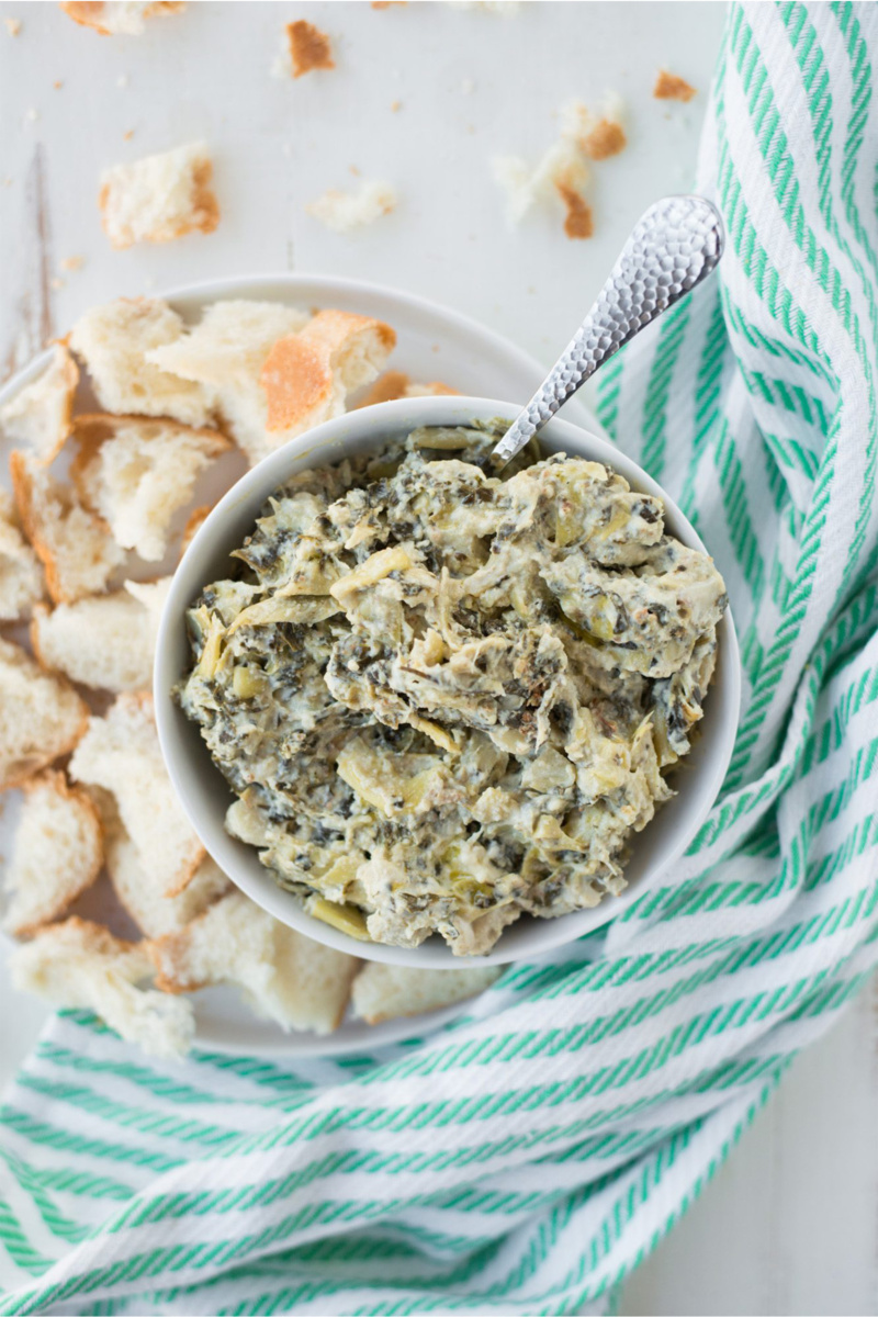 a bowl of vegan spinach artichoke dip served with chunks of bread