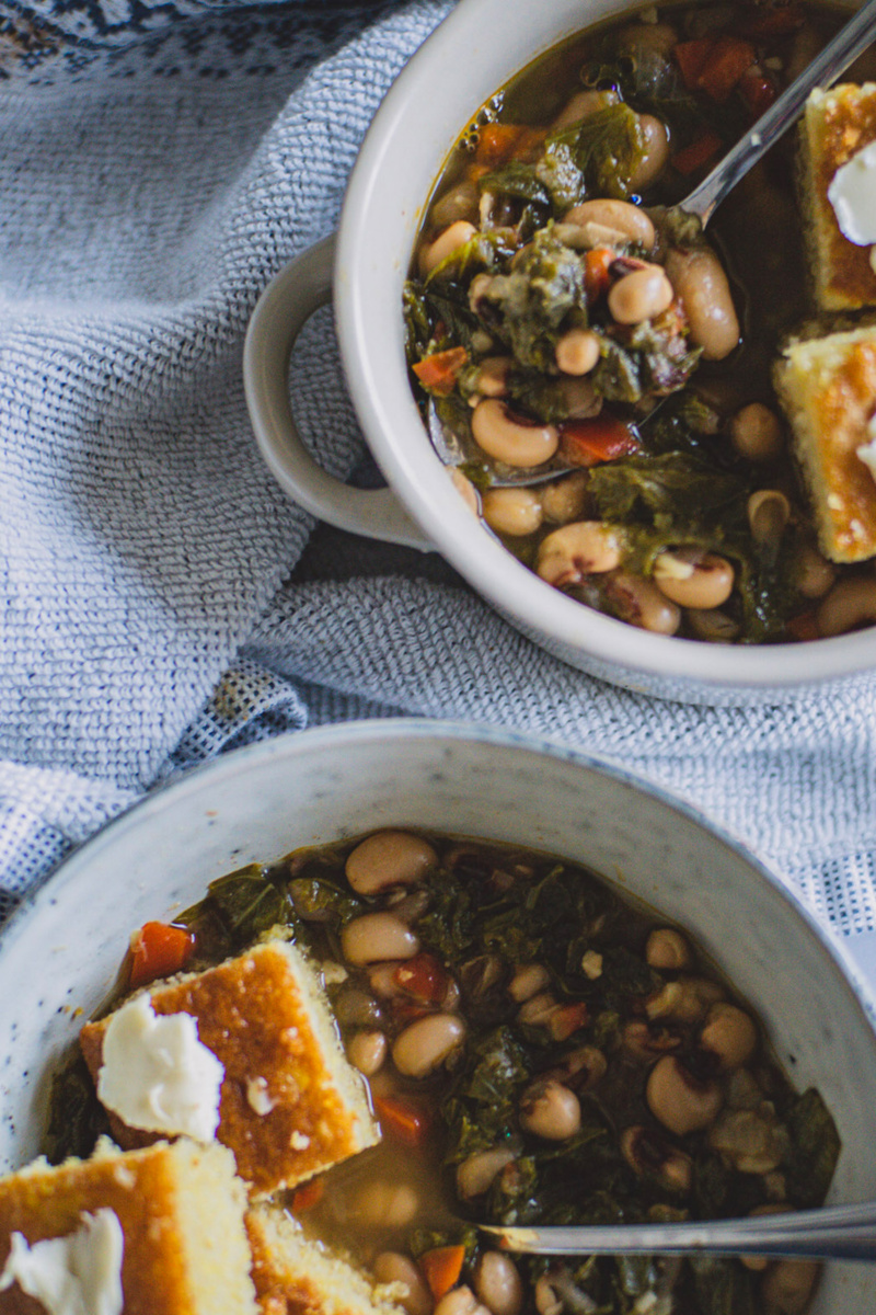 two bowls of black eyed peas and greens served with biscuits