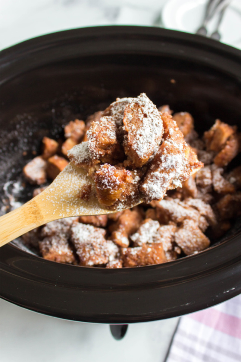 a wooden spoon scooping out a serving of french toast casserole from a crockpot