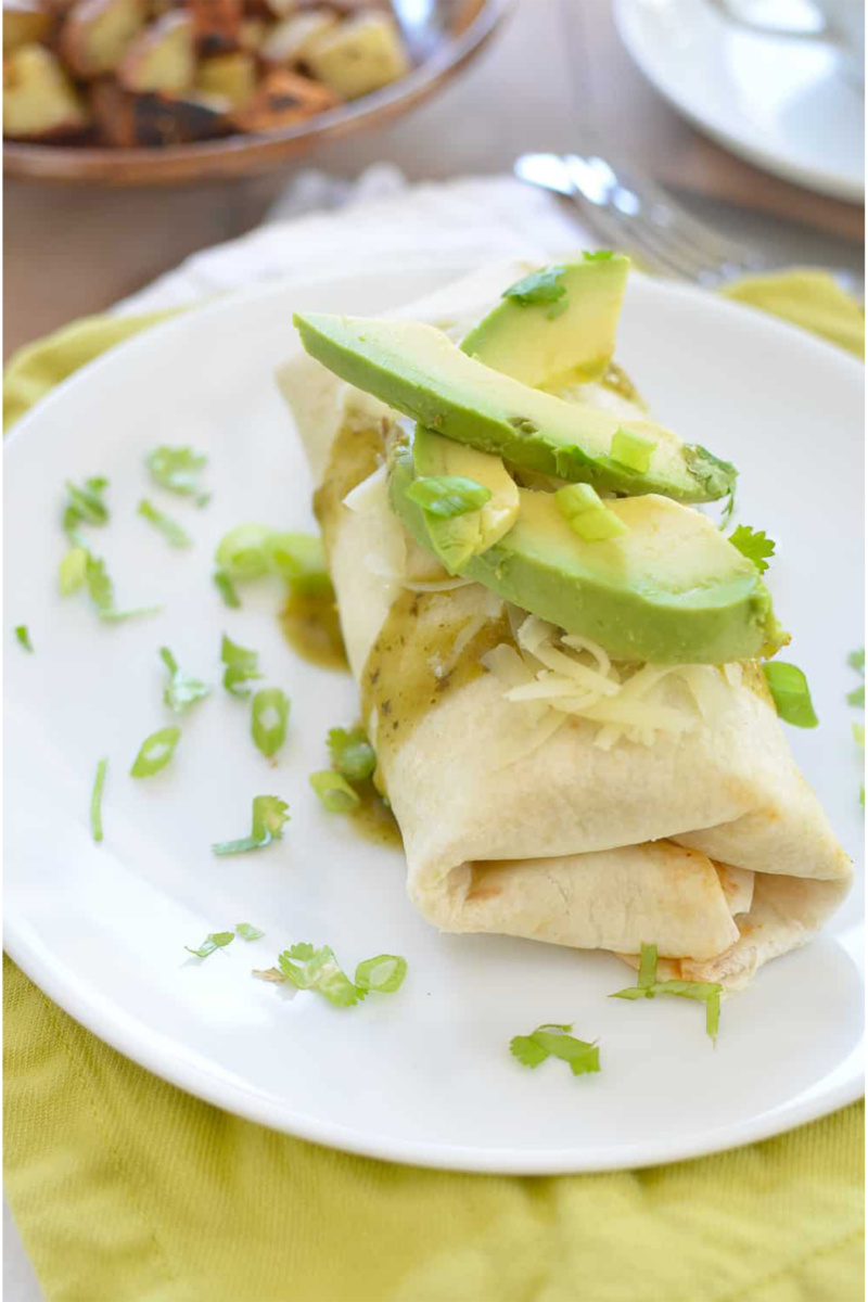 a breakfast burrito topped with salsa and sliced avocado