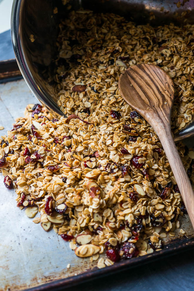 a crockpot pouring out granola onto a cookie sheet lined with parchment paper