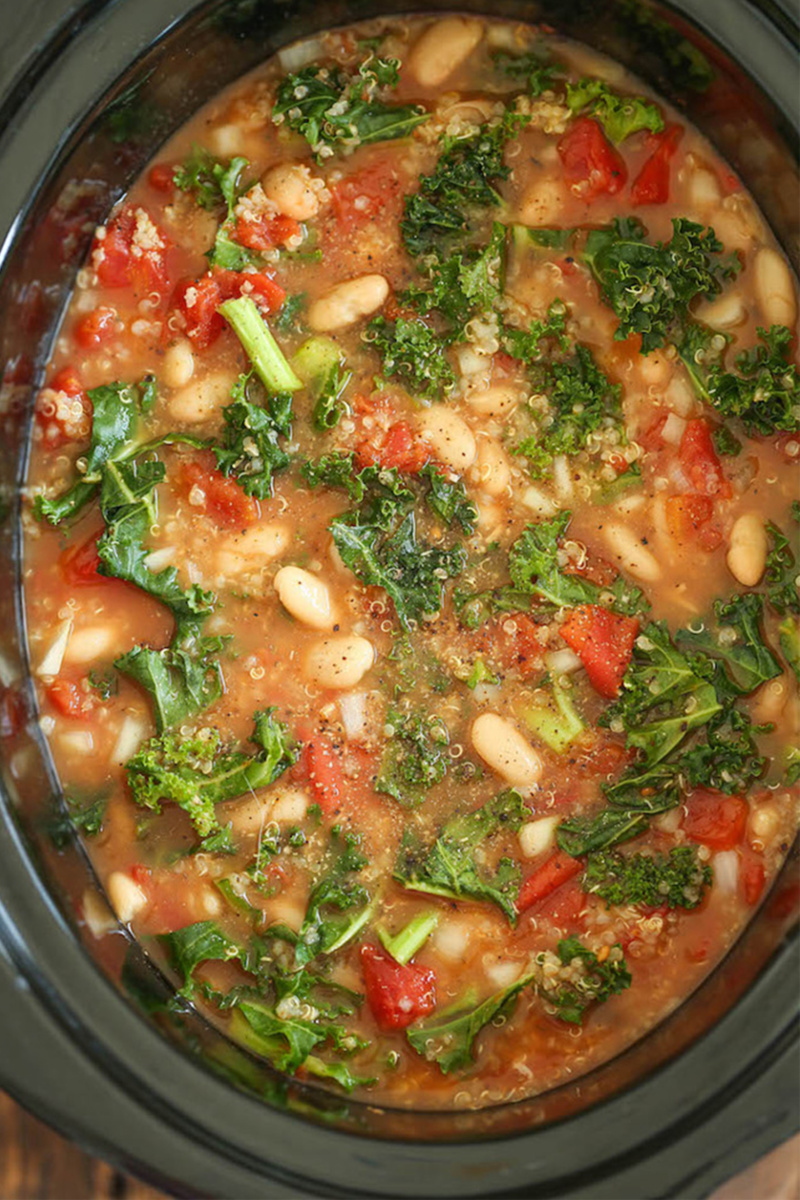 a kale, tomato and white bean soup being cooked in a slow cooker