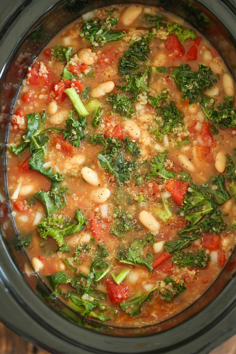a kale, tomato and white bean soup being cooked in a slow cooker