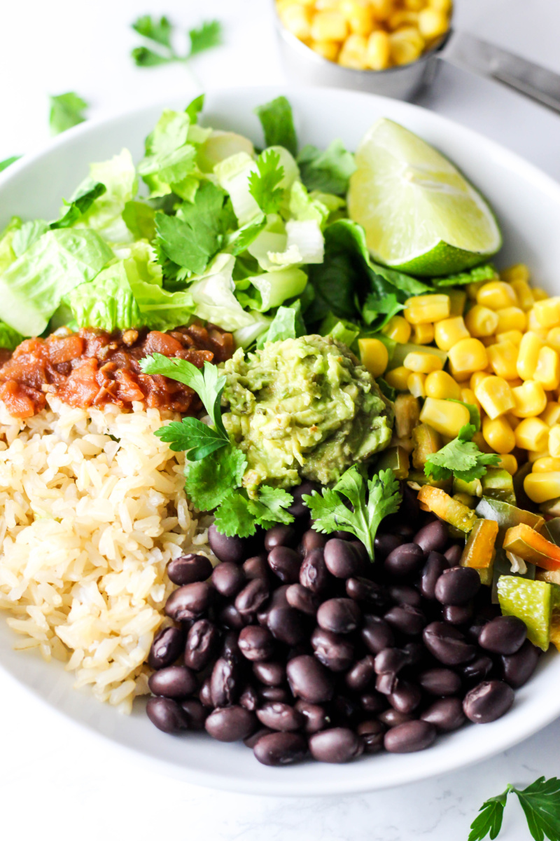 A vegan burrito bowl made with rice, salsa, corn, black beans, lettuce and guacamole