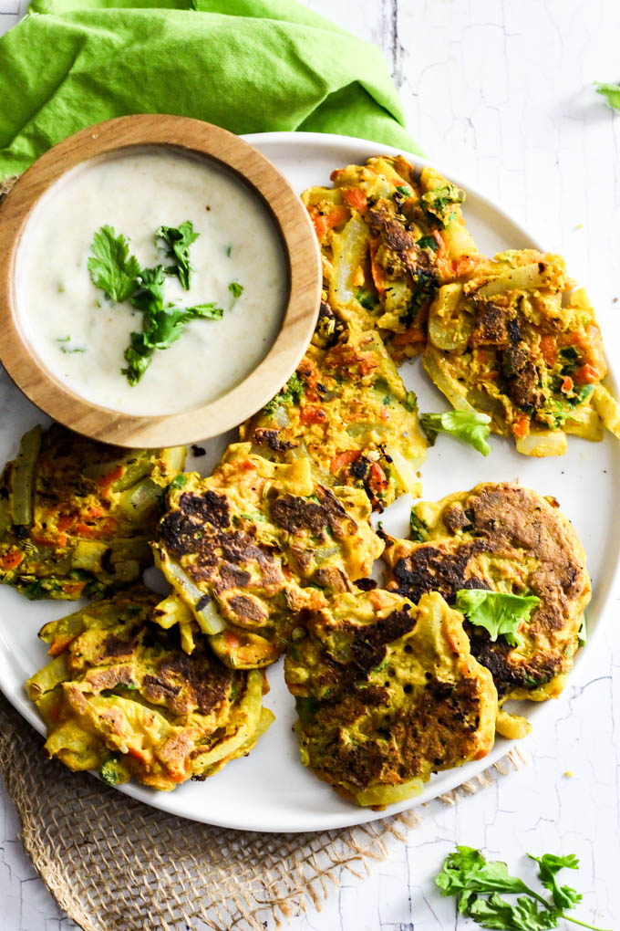 Add these Crispy Onion & Carrot Fritters to dinner for a flavorful, vegetable-packed side dish! A dollop of cumin yogurt tops it off. Vegan & gluten-free!