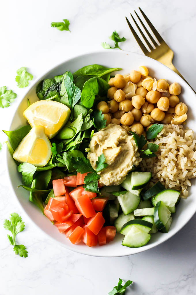 a salad with spinach, chickpeas, rice, cucumber, tomatoes, parsley hummus and lemon wedges on the side
