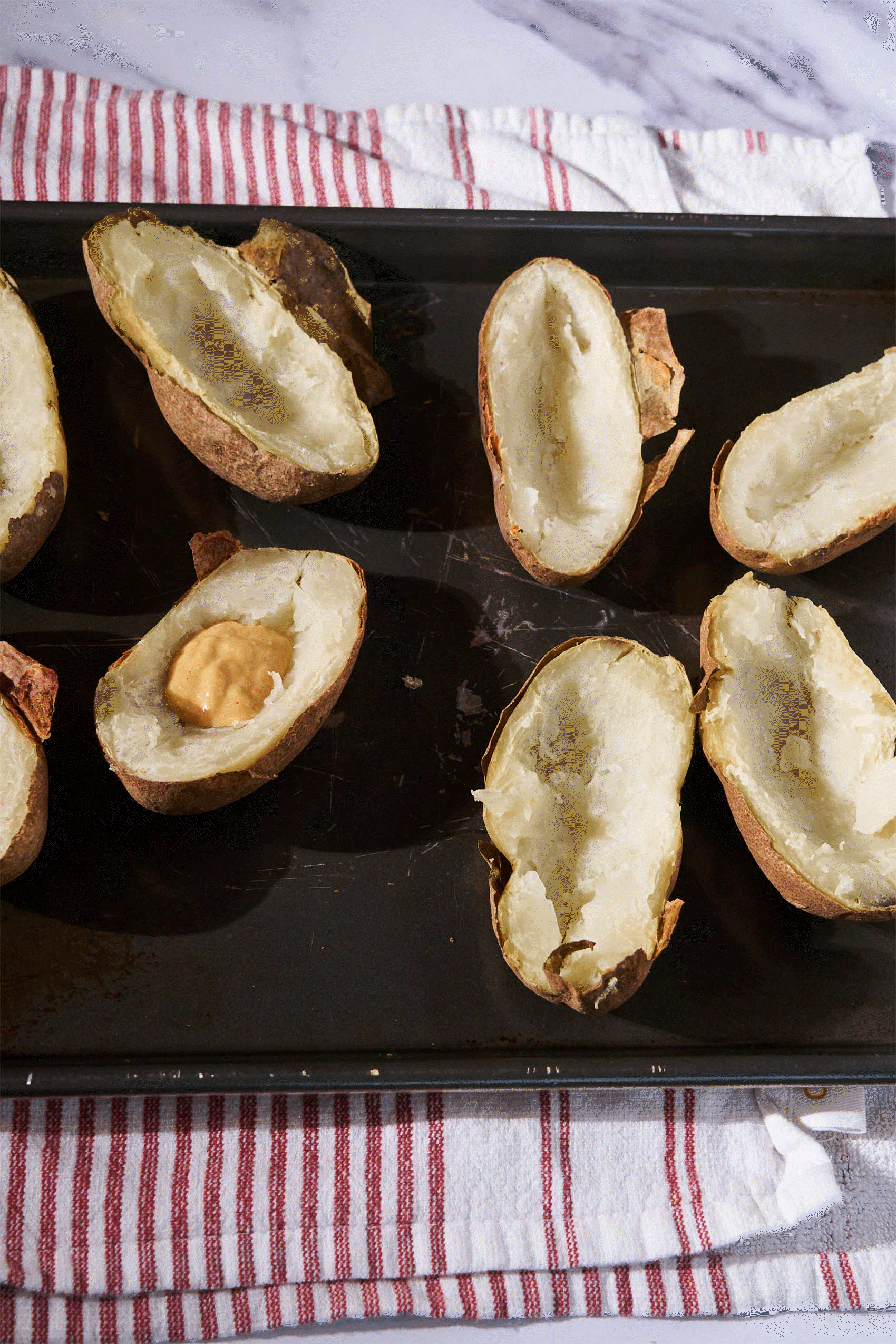 a sheet tray of hallowed out baked potatoes being filled with vegan cheese sauce