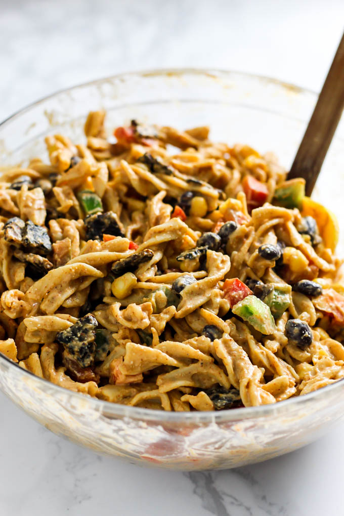 A large mixing bowl filled with a pasta salad containing cashew cream sauce, black beans, corn, peppers and vegan bacon