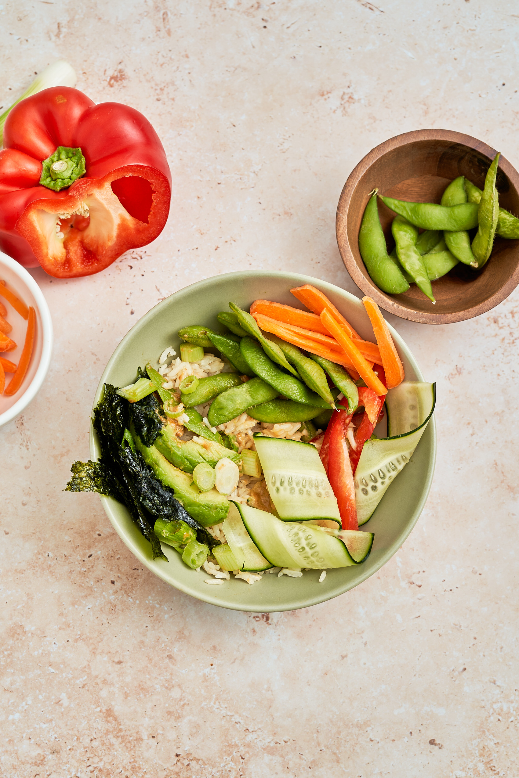 a lunch bowl containing rice, edamame, carrots, bell peppers, nori and avocado
