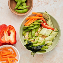 a vegan edamame bowl filled with brown rice, carrots, cucumber, bell pepper and avocado