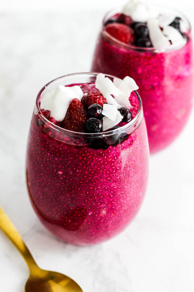 a glass filled with a serving of strawberry beet chia pudding topped with strawberries, blueberries and coconut flakes