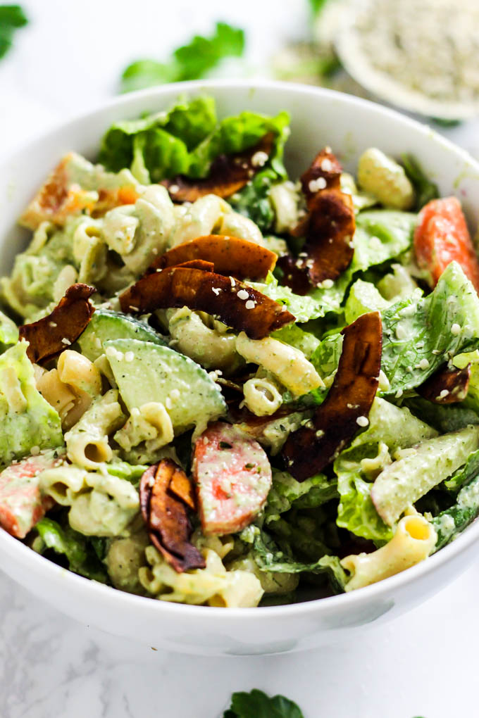 A bowl of pasta salad with lettuce, carrots, radishes, peppers, coconut bacon, pasta and dairy free ranch