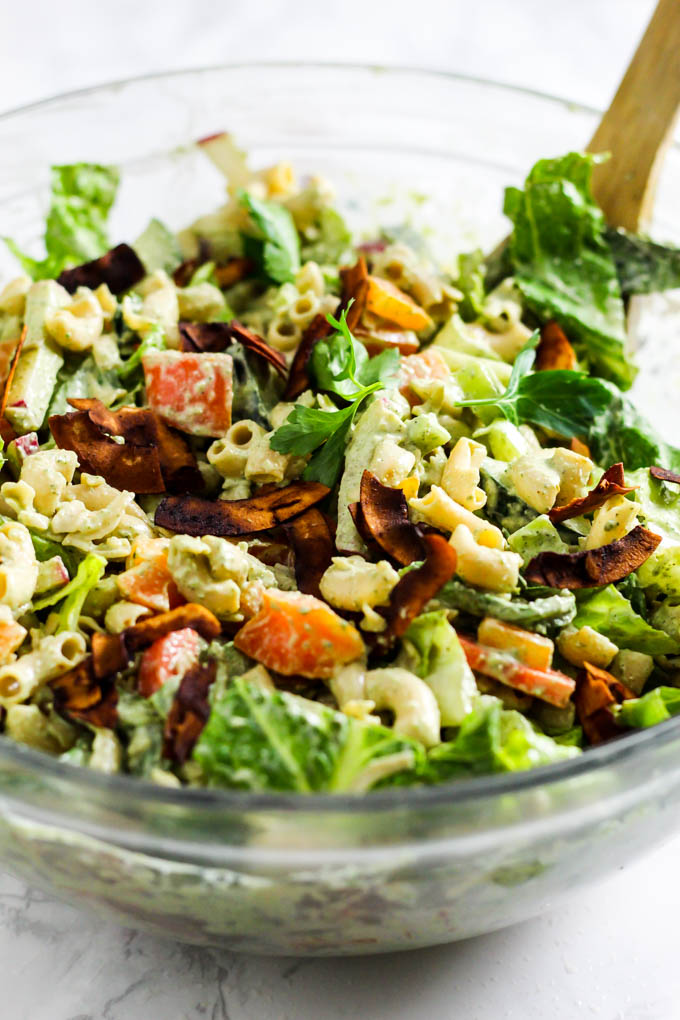 A large bowl of pasta salad being mixed by a wooden spoon